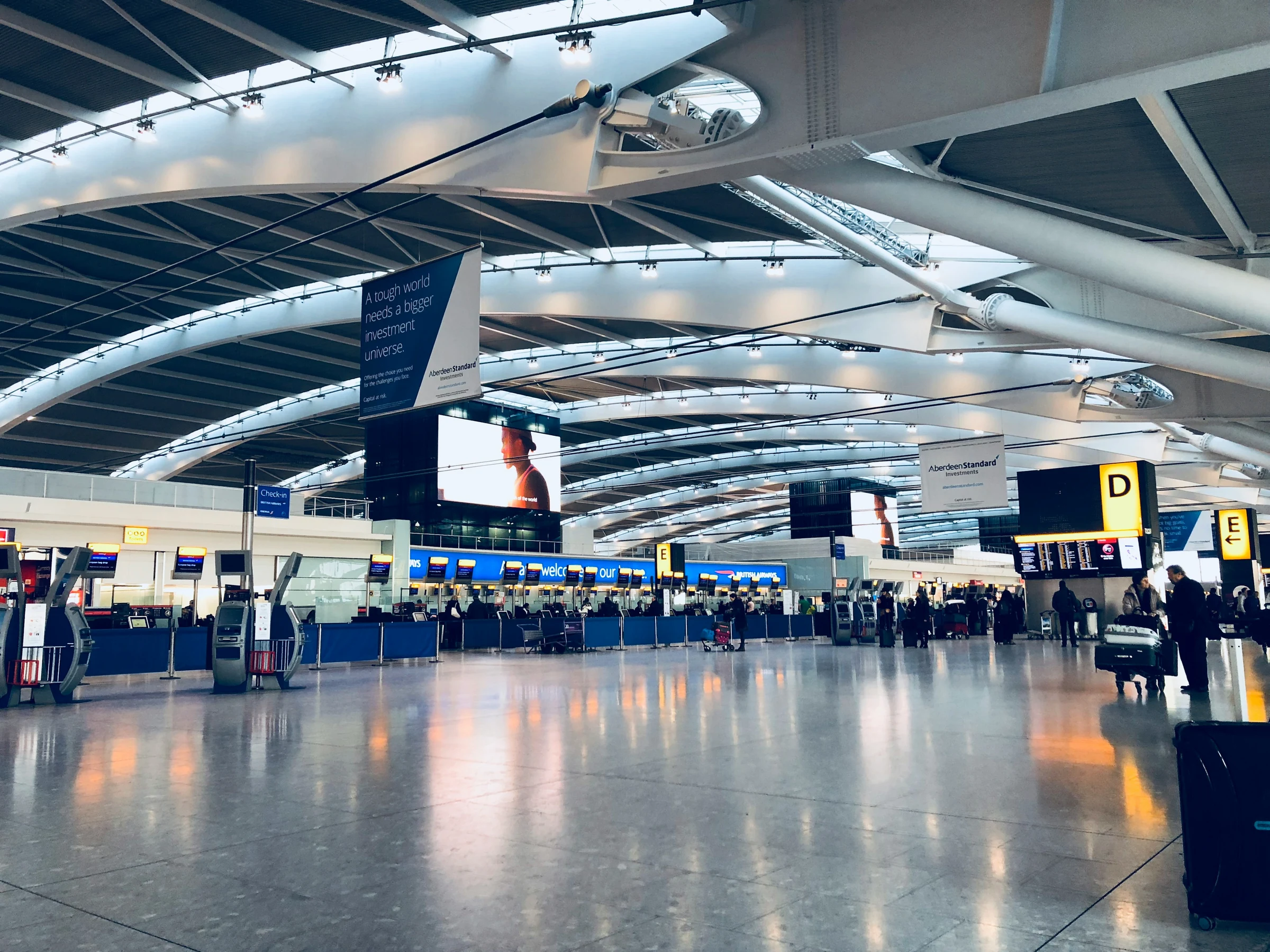 The departures hall of a major European international airport, with travellers moving through the terminal.
