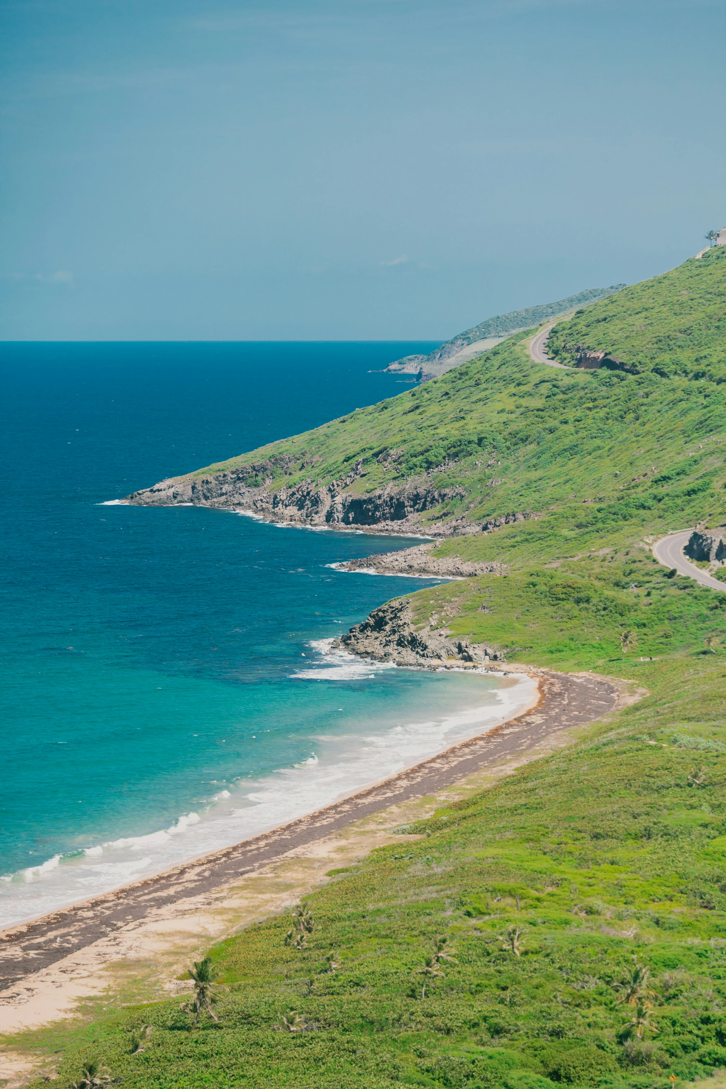 A winding road traversing a lush green coastal hillside in the Eastern Caribbean.