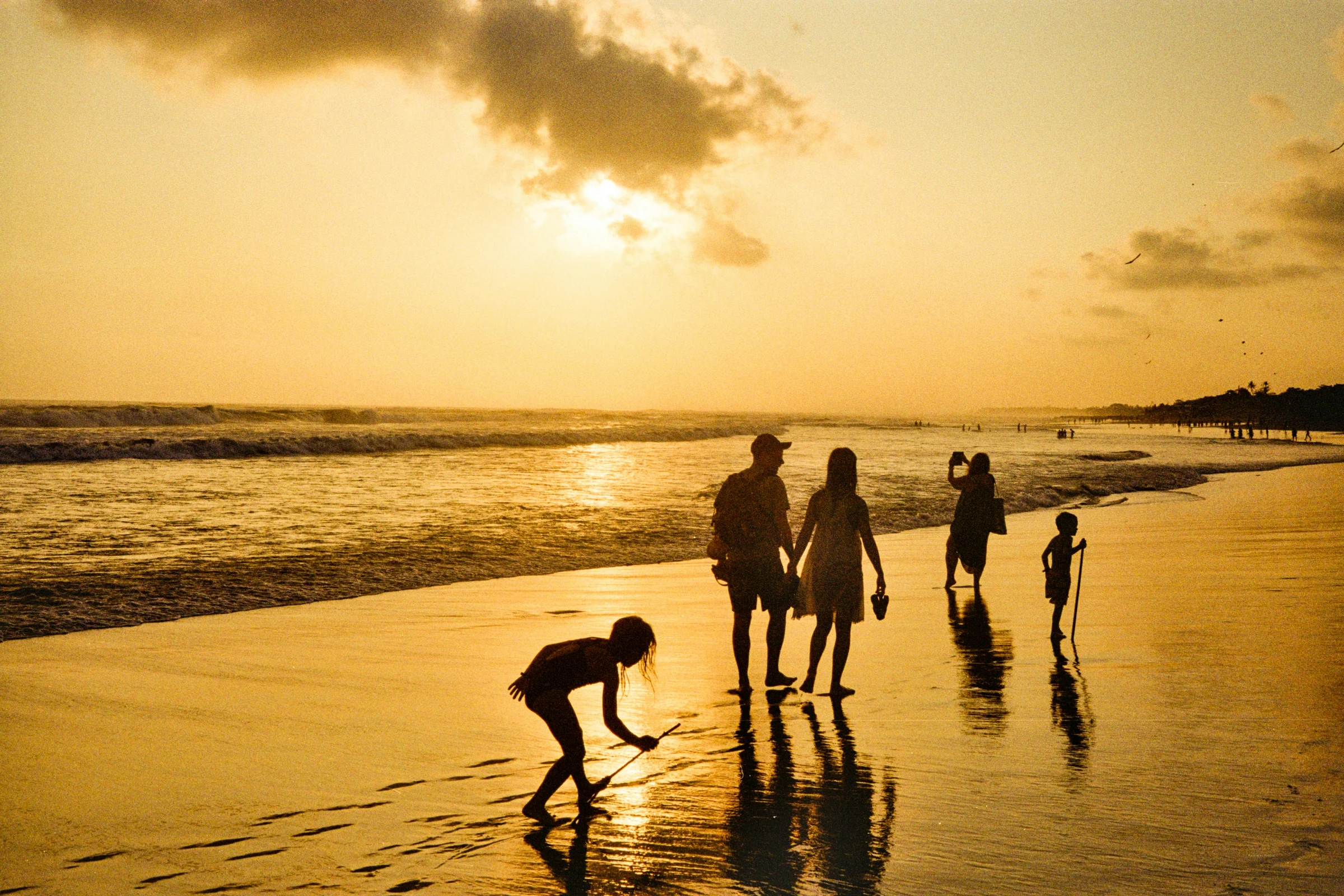 A Caribbean family-coded scene — a wide beach at golden hour, framed by palms.