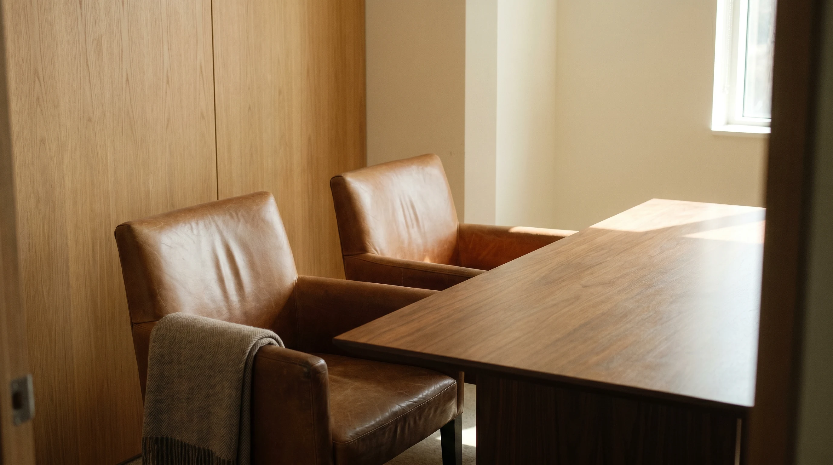 Two cognac leather chairs at a walnut conference table, intimate meeting room with wood panelling